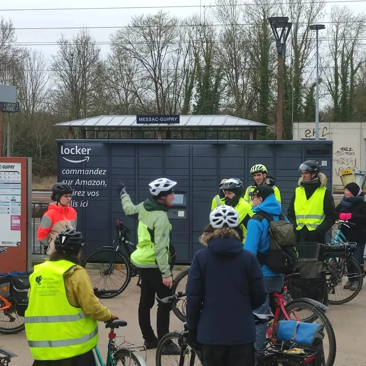 Des cyclistes en gilet jaune rassemblés devant la gare de Messac-Guipry, l'un d'eux montre la direction