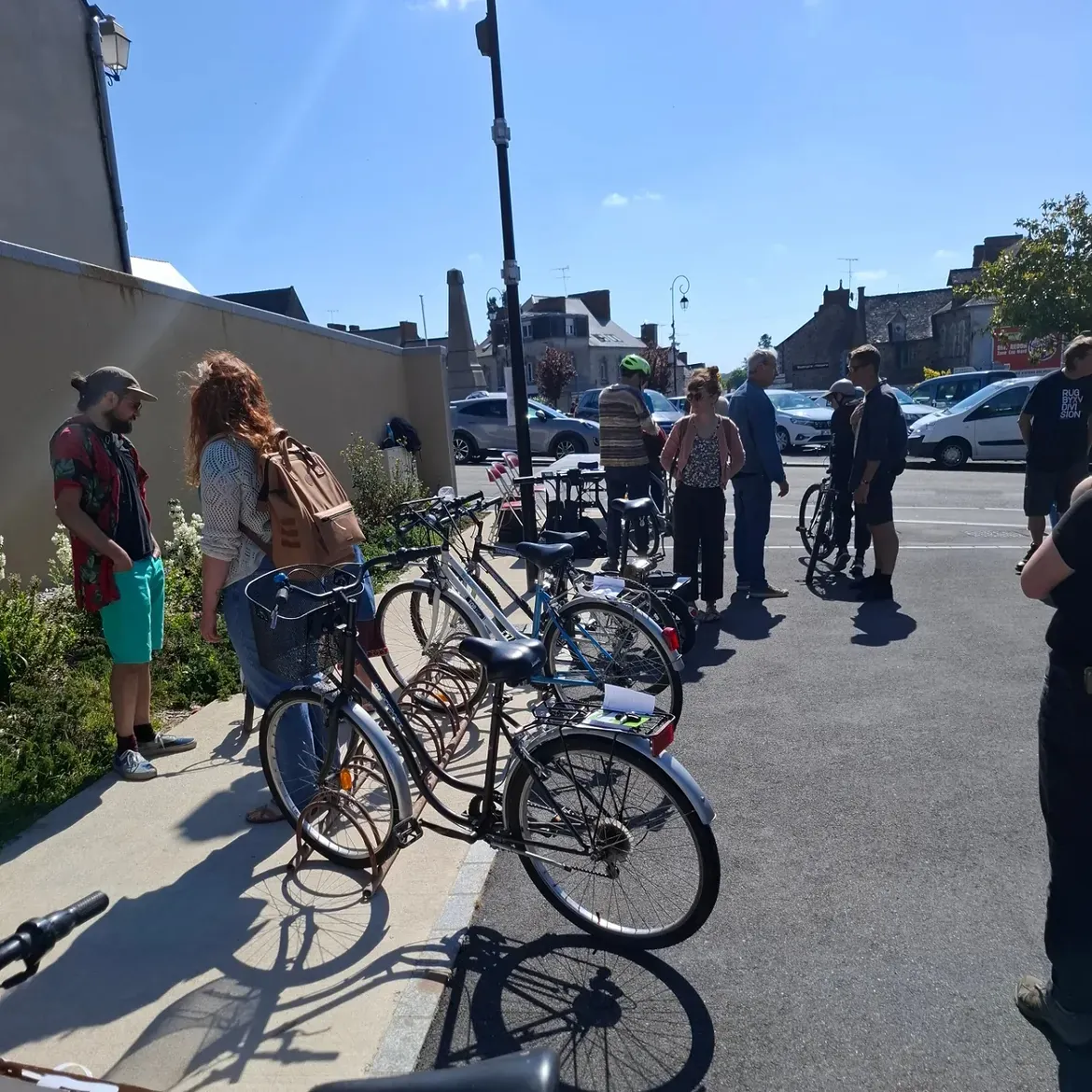 Des visiteurs entre les vélos garés le long d'un mur, sous un grand ciel bleu