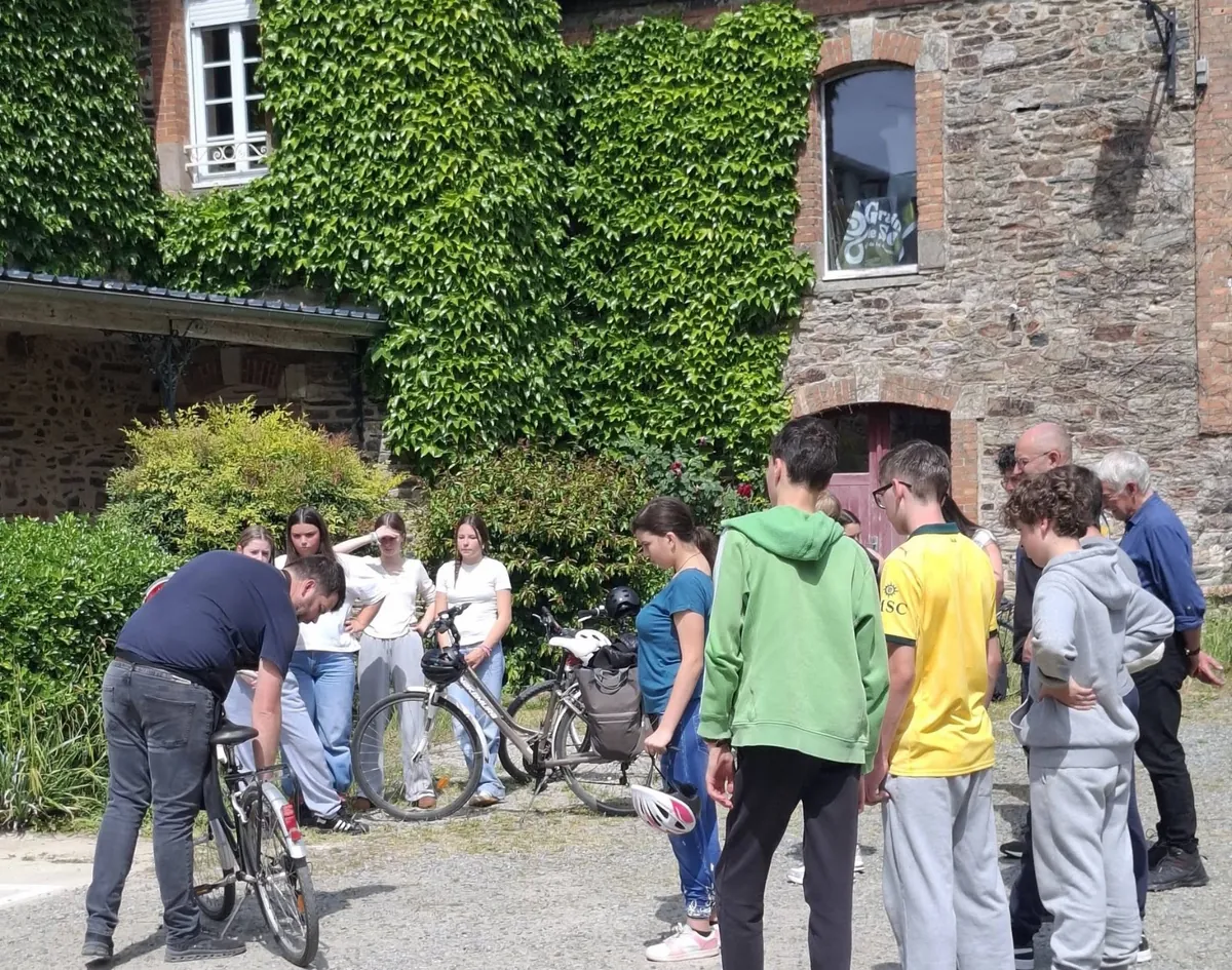 Des collégiens et des bénévoles autour de vélos retournés, devant un bâtiment en pierre, pendant l'atelier mécanique