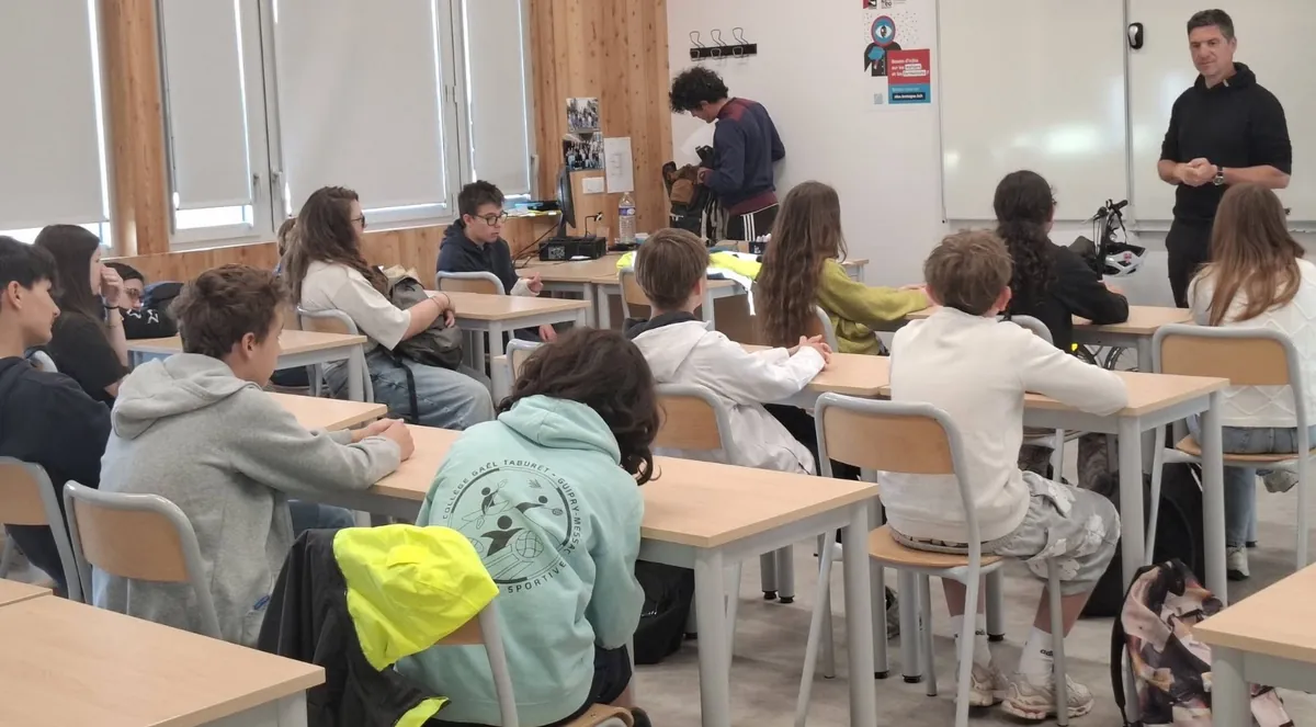 Une salle de classe : les élèves assis à leurs tables écoutent un intervenant