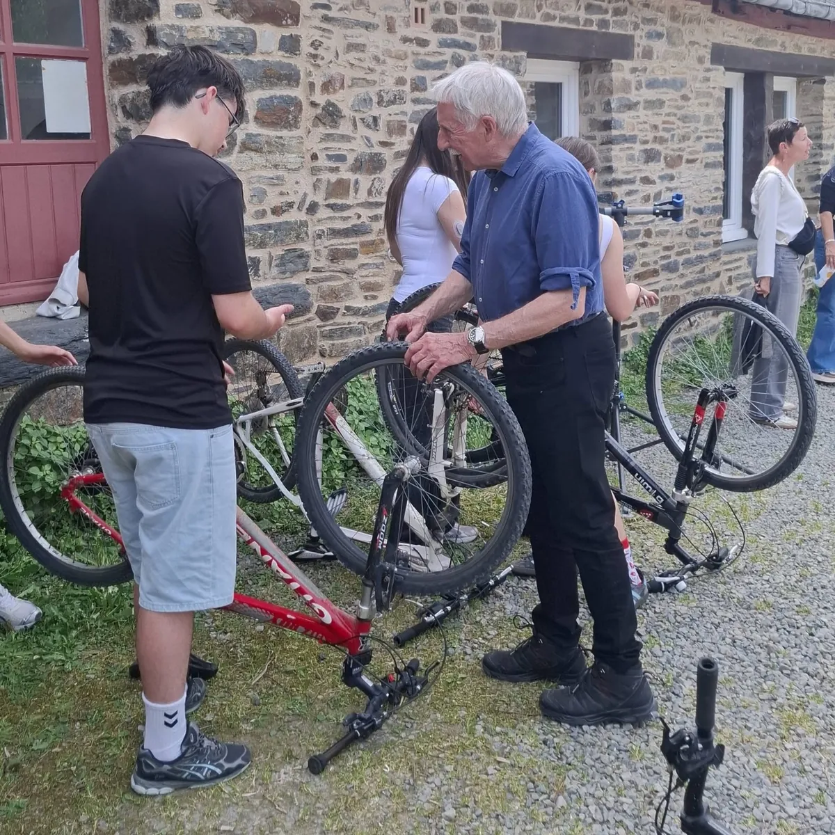 Un bénévole règle un vélo avec un élève, d'autres élèves et vélos autour