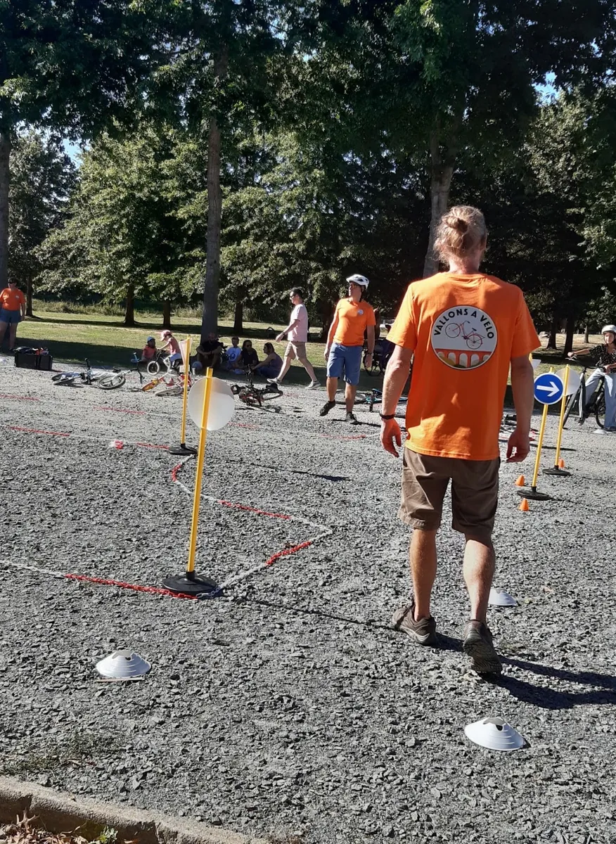 Un bénévole de dos, en tee-shirt orange Vallons à vélo, sur un parcours de maniabilité balisé de piquets et de plots