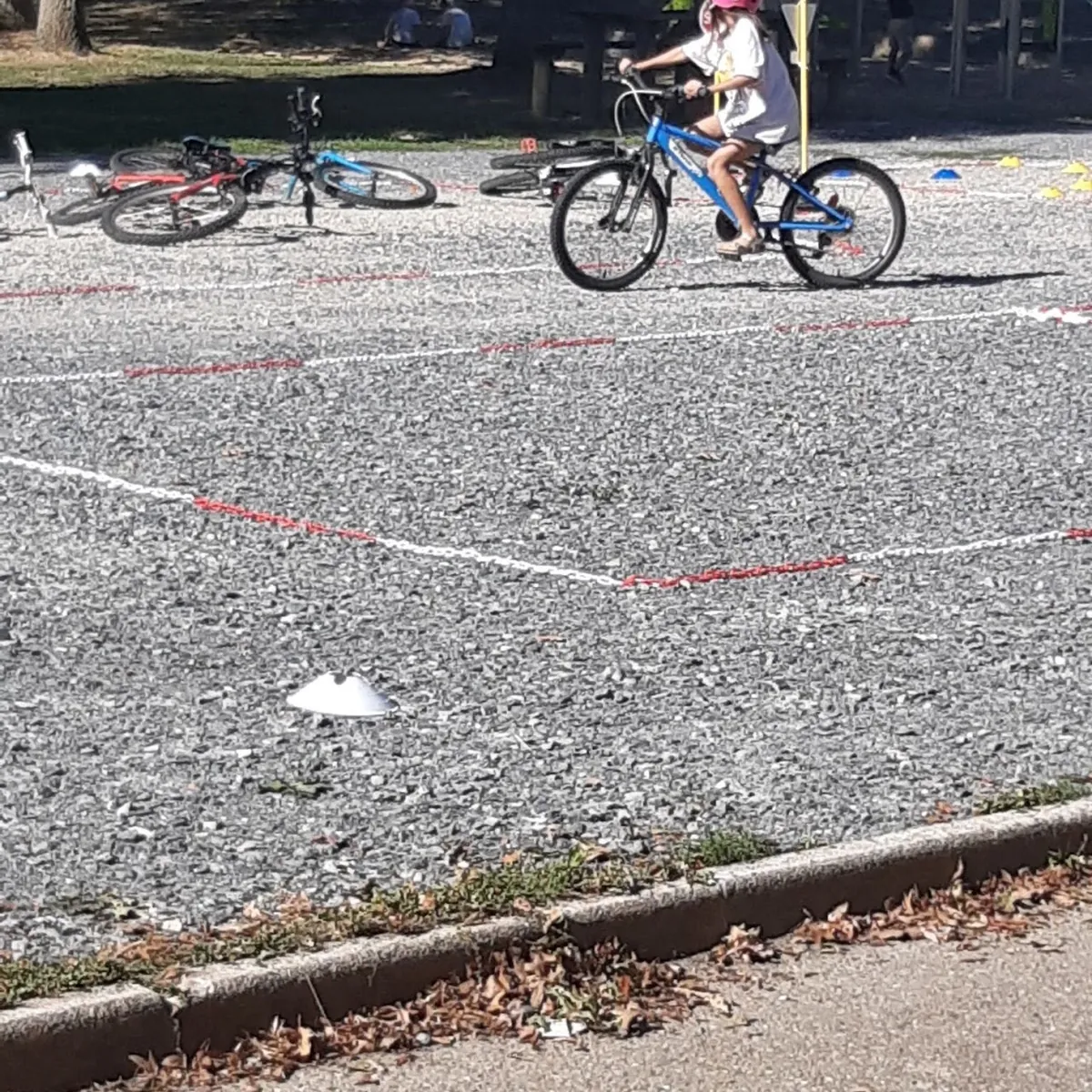 Un enfant casqué roule sur le parcours, d'autres vélos posés sur le gravier