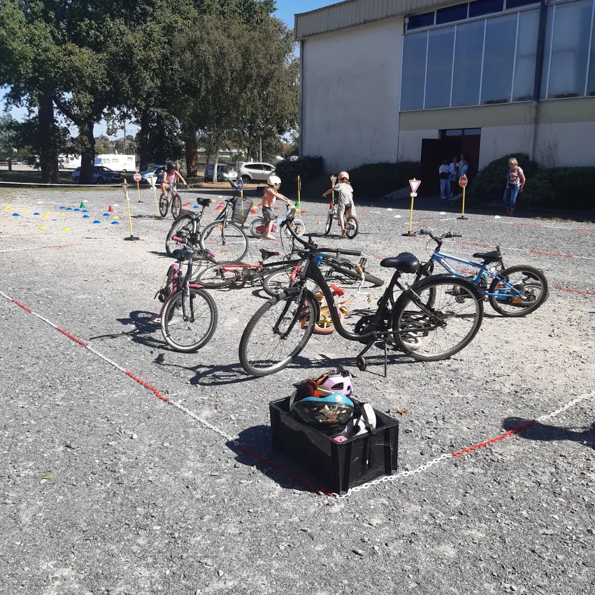 Des vélos d'enfant et une caisse de casques au premier plan, des enfants qui roulent sur le parcours au fond